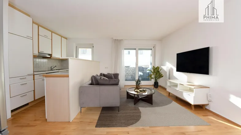 Helles, offenes Wohnzimmer mit integrierter Küche, Holzboden und Zugang zum Balkon.