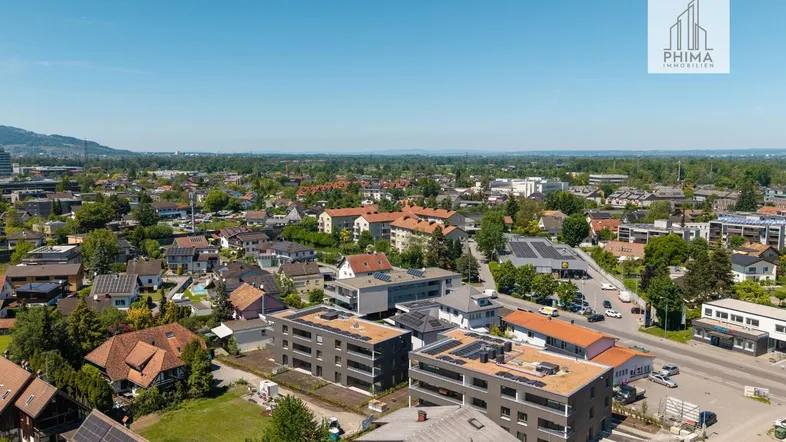 Luftaufnahme einer Wohnsiedlung mit modernen Gebäuden und grüner Umgebung unter blauem Himmel.