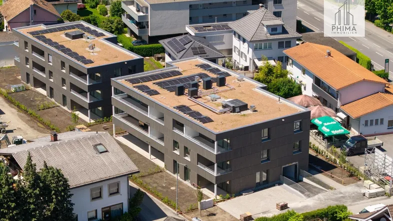 Luftaufnahme von zwei modernen Wohngebäuden mit Photovoltaikanlagen auf den Flachdächern in einer städtischen Umgebung.