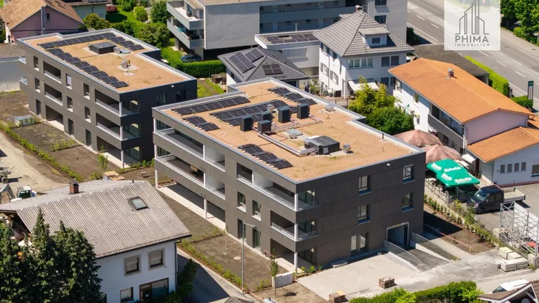 Luftaufnahme von zwei modernen Mehrfamilienhäusern mit Flachdächern und Solaranlagen in einer Wohngegend.