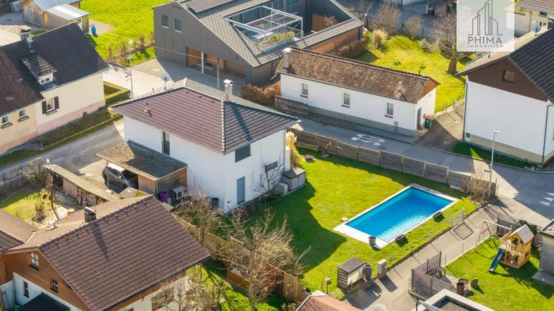 Luftaufnahme eines Wohngebiets mit Einfamilienhäusern, gepflegten Gärten und einem privaten Swimmingpool.
