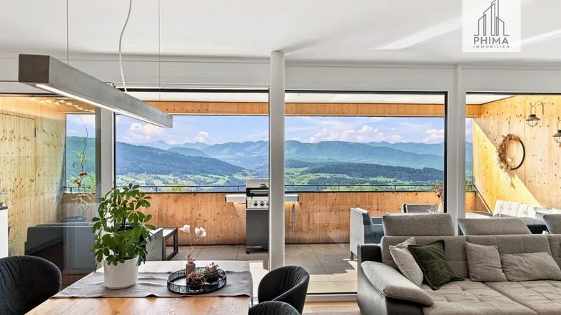 Heller Wohn- und Essbereich mit Holzboden, gemütlichem Sofa und beeindruckendem Bergblick durch große Fenster.