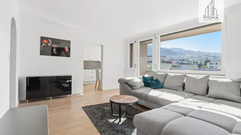 Helles Wohnzimmer mit großem Sofa, Holzboden und Blick auf die umliegende Landschaft.