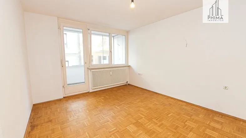 Helles Zimmer mit Parkettboden und Zugang zu einem kleinen Balkon, ideal als Wohn- oder Schlafbereich.