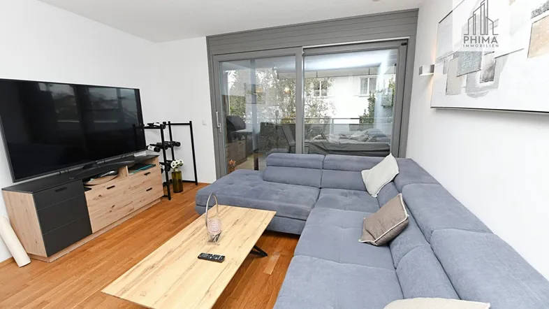 Helles Wohnzimmer mit großem Sofa, TV-Möbel und Zugang zum Balkon.