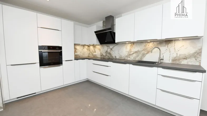 Moderne Einbauküche mit weißen Fronten, dunkler Arbeitsplatte und gemusterter Rückwand.