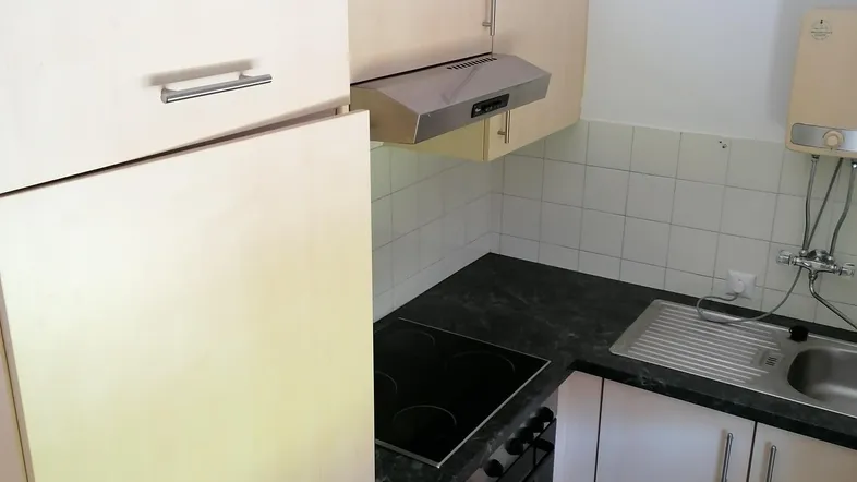 Kleine Küche mit hellen Holzschränken, dunkler Arbeitsplatte und integrierten Geräten.