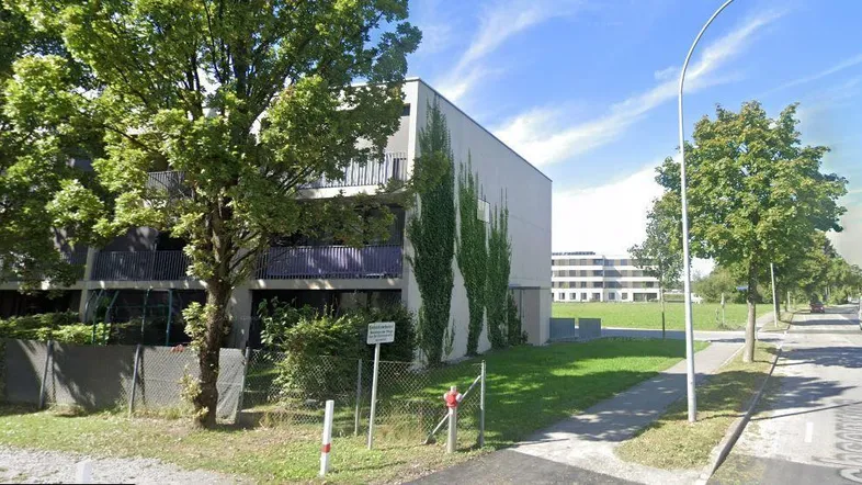 Modernes Mehrfamilienhaus mit schlichter Fassade und begrünten Balkonen an einer Straße.