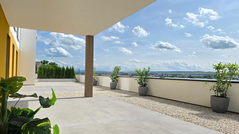 Geräumige Dachterrasse mit hellen Fliesen, Zierkies und weitem Blick in die Landschaft.