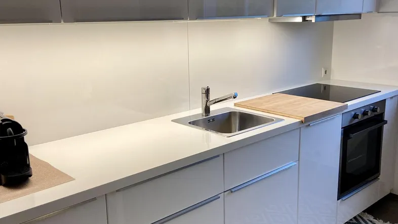 Moderne Küche mit weißen Hochglanzfronten, Spüle und Kochfeld, ergänzt durch einen gemusterten Teppich.