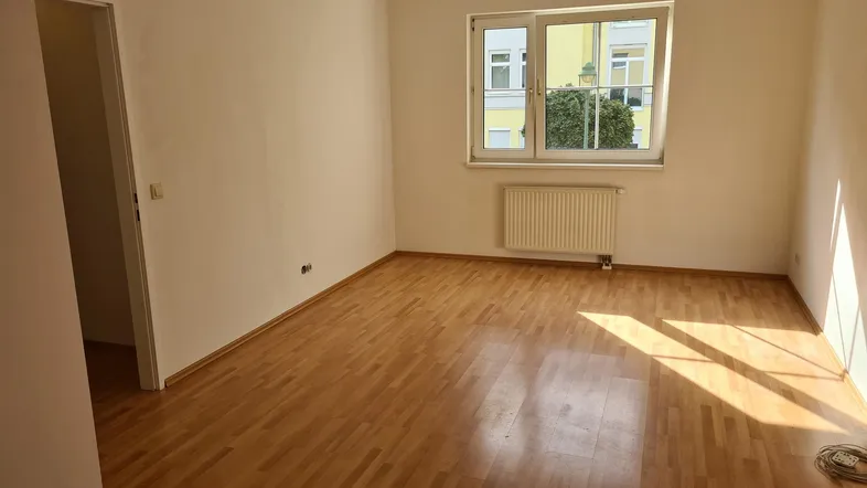 Helles Zimmer mit Parkettboden und Fenster, das viel Tageslicht hereinlässt.