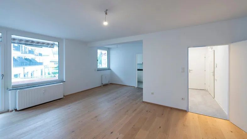 Helles Wohnzimmer mit neuem Parkettboden und Zugang zu weiteren Räumen.