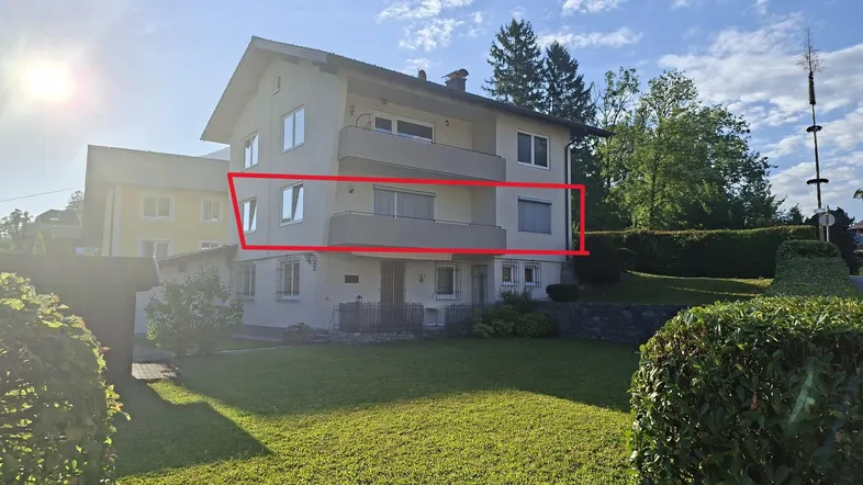 Mehrstöckiges Wohngebäude mit Balkonen und gepflegtem Vorgarten unter blauem Himmel.