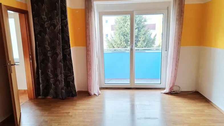 Helles Zimmer mit Parkettboden und Zugang zu einem Balkon, ideal als Wohn- oder Schlafbereich.