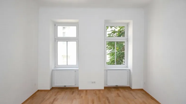 Helles Zimmer mit zwei Fenstern, Heizkörpern und schönem Parkettboden, bereit zur Einrichtung.