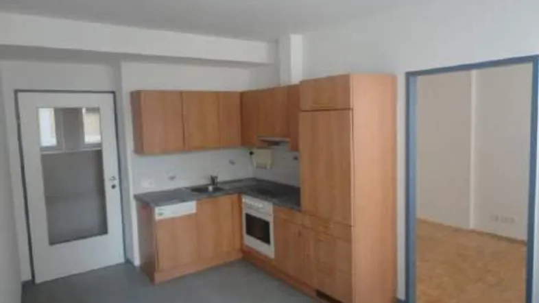Funktionale Einbauküche mit Holzfronten, grundlegenden Geräten und Fliesenboden in einem hellen Raum.