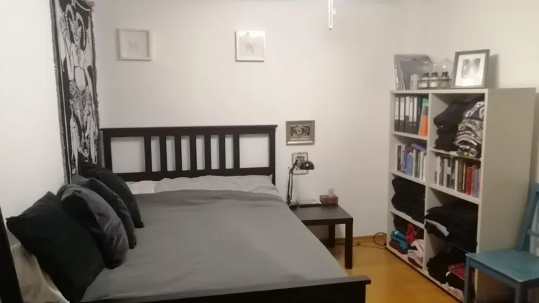 Schlafzimmer mit einem Doppelbett, Nachttisch, Leselampe und einem praktischen Bücherregal.