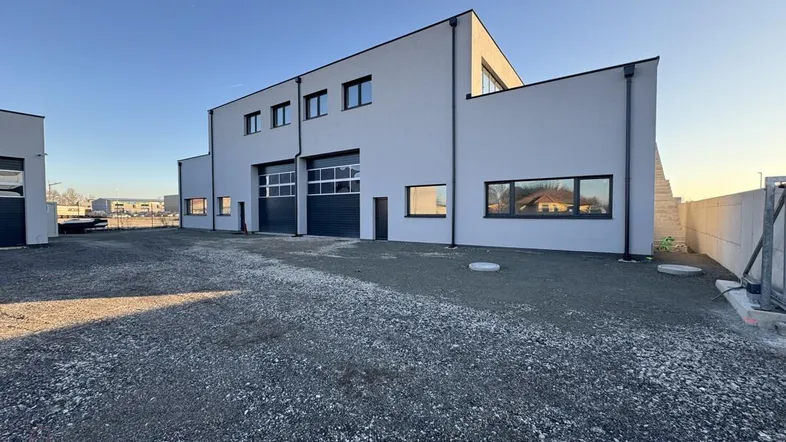 Modernes Geschäftsgebäude mit heller Fassade und großem Schotterparkplatz unter klarem Himmel.