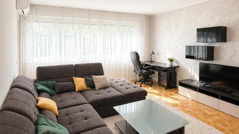 Helles Wohnzimmer mit großem Ecksofa, Schreibtisch und Klimaanlage, ideal zum Entspannen und Arbeiten.