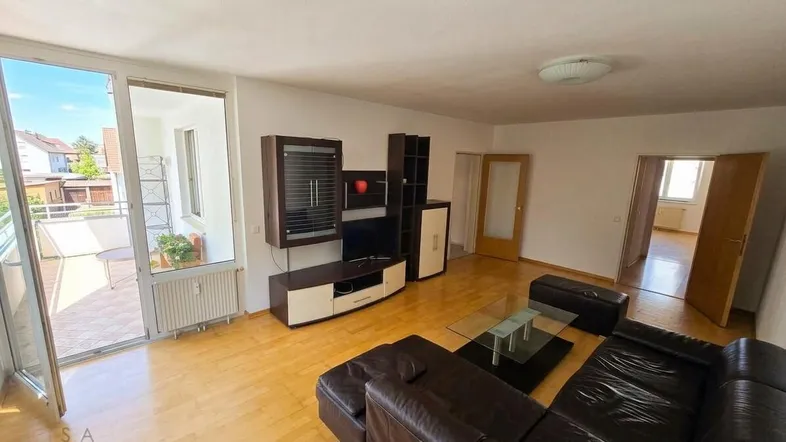Helles Wohnzimmer mit dunklem Ledersofa, Holzfußboden und direktem Zugang zum sonnigen Balkon.