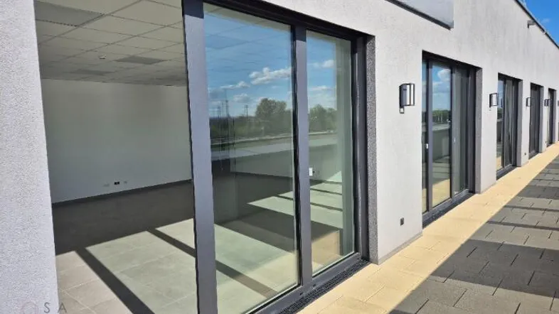 Eine moderne Terrasse mit großen Glasschiebetüren, die zu den Innenräumen führen, und einem gepflasterten Boden.