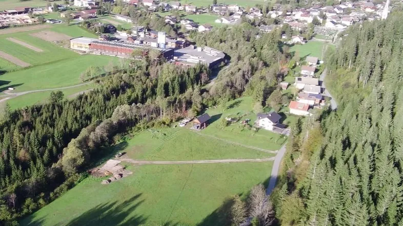Luftaufnahme eines Dorfes umgeben von Wäldern und grünen Wiesen mit Fernblick.