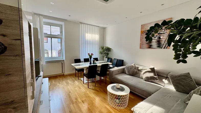 Helles Wohn- und Esszimmer mit Holzparkettboden, bequemer Couch und modernem Esstisch.