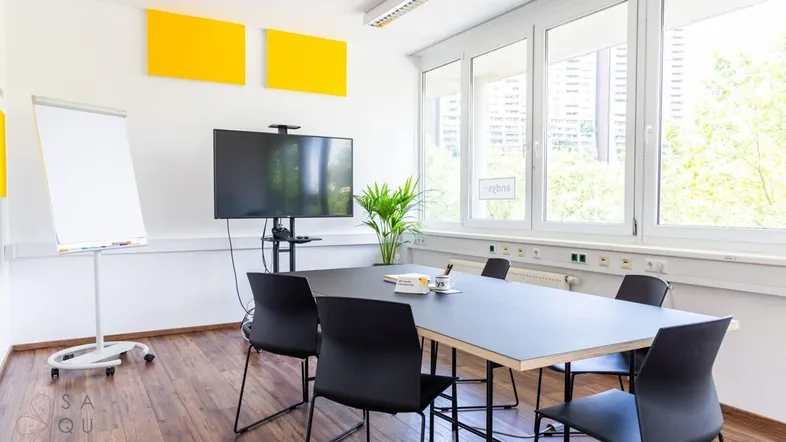 Moderner Konferenzraum mit großem Bildschirm, Whiteboard und Blick ins Grüne durch die Fenster.