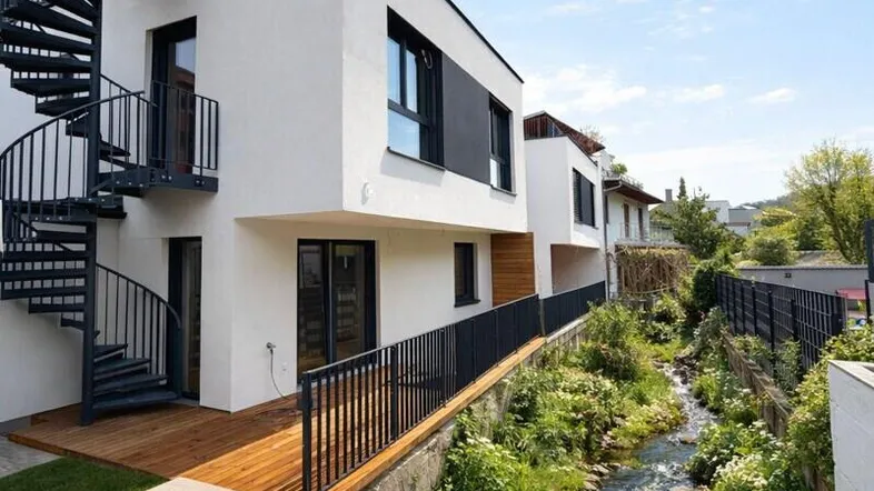 Moderne Reihenhäuser mit weißer Fassade, schwarzer Wendeltreppe und einem Bachlauf im Garten.