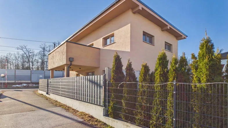 Modernes Einfamilienhaus mit schräger Dachlinie und gepflegter Außenanlage unter blauem Himmel.