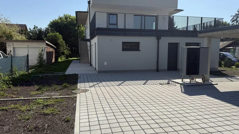 Moderne Neubau-Doppelhaushälfte mit gepflastertem Vorplatz und Außentreppe zum Obergeschoss.