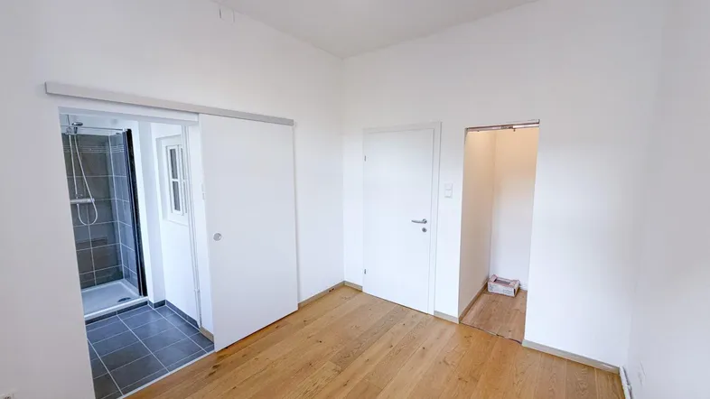 Helles Schlafzimmer mit Holzboden und direktem Zugang zu einem modernen Duschbad.