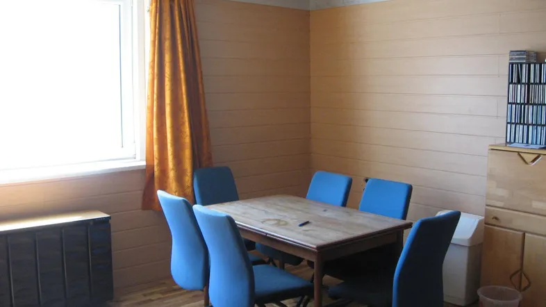 Gemütliches Esszimmer mit Holztisch, blauen Stühlen und Holzvertäfelung an den Wänden.