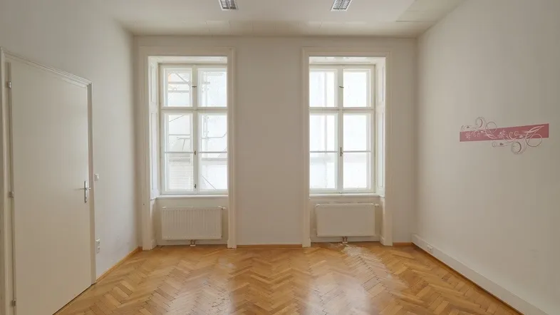 Heller Büroraum mit Fischgrätparkett, zwei großen Fenstern und weißen Wänden, ideal für Arbeitsbereiche.