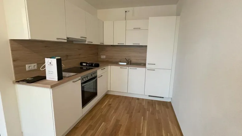 Moderne Einbauküche mit weißen Schränken, Holzoptik-Arbeitsplatte und Parkettboden in neuwertigem Zustand.