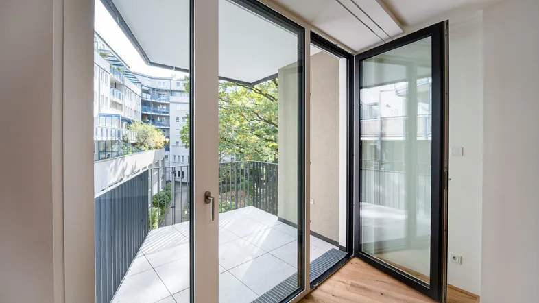 Heller Wohnraum mit Holzboden und großen Fenstern, die Zugang zu einem Balkon bieten.