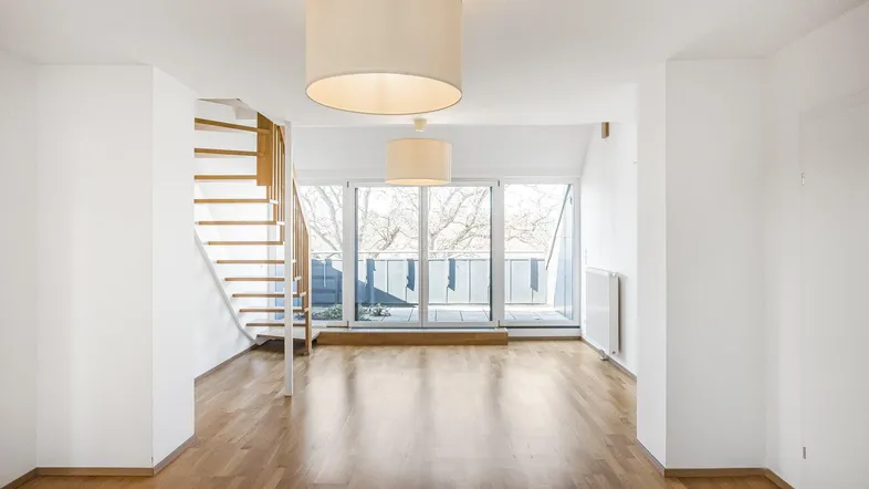 Helles Wohnzimmer mit Holzparkett, Wendeltreppe und Zugang zu einem Balkon.