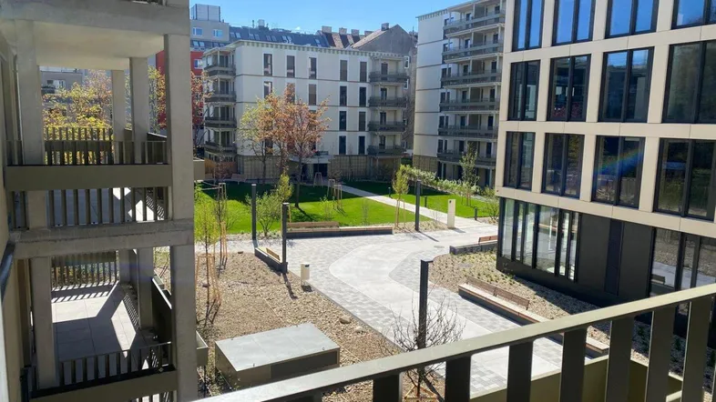 Blick vom Balkon auf den begrünten Innenhof mit modernen Wohngebäuden und Sitzgelegenheiten.