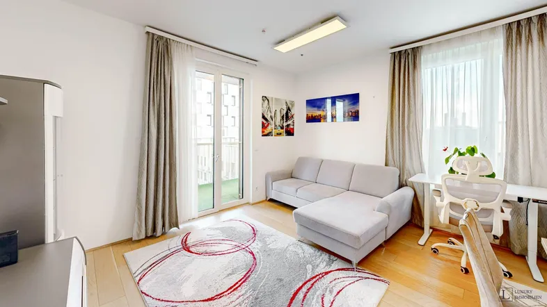 Helles Wohnzimmer mit Sofa, Schreibtisch und Zugang zu einem kleinen Balkon.