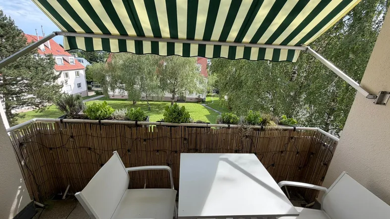 Möblierter Balkon mit gestreifter Markise und Blick auf den grünen Innenhof.