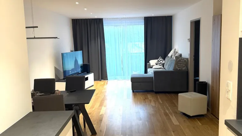 Helles, offenes Wohnzimmer mit Holzboden, Sofa und Zugang zu einem Balkon.
