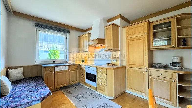 Gemütliche Küche mit Holzschränken, integrierter Sitzbank, Fenster und Parkettboden.
