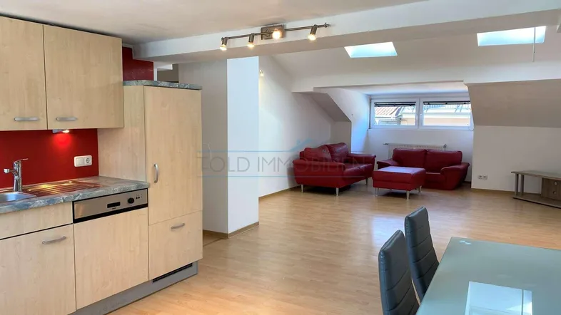 Heller offener Wohn- und Essbereich mit integrierter Küche, Esstisch und rotem Sofa unter Dachschrägen.