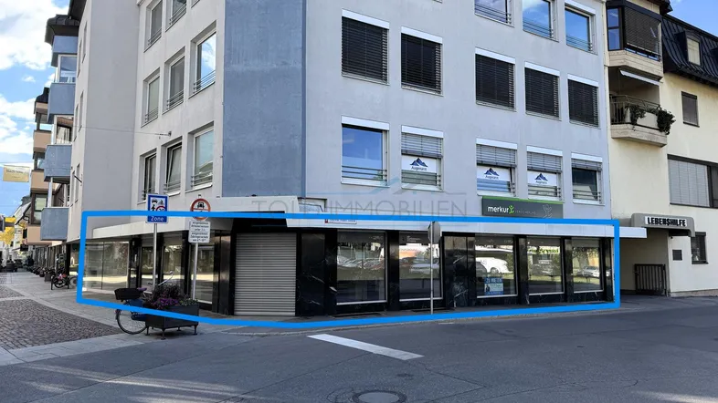 Gebäudeansicht mit hervorgehobener Ladenfläche im Erdgeschoss und großen Schaufenstern zur Straße.