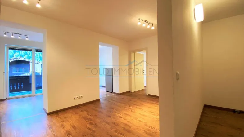 Heller Wohnbereich mit Laminatboden und Zugang zu einem Balkon mit Bergblick.