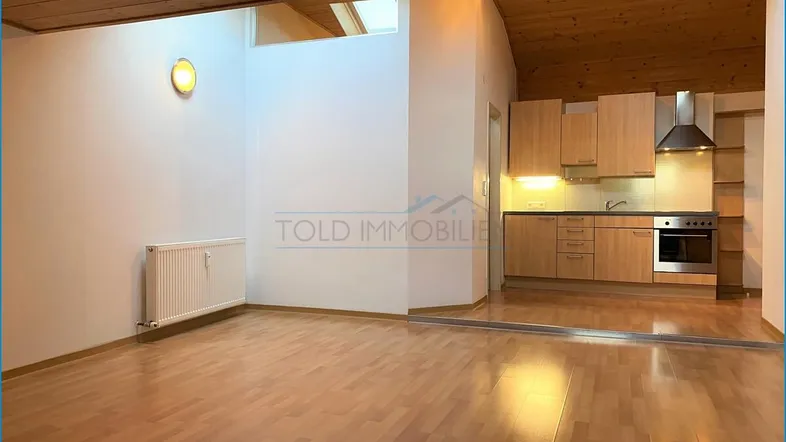 Helles Wohnzimmer mit Holzbalkendecke, Dachfenster und integrierter Küche im offenen Wohnbereich.
