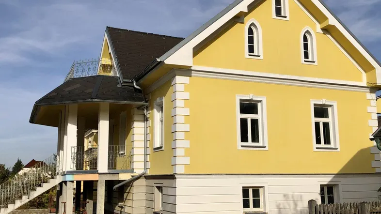 Gelbe Fassade eines Hauses mit weißer Stuckverzierung und Balkon im Bau.
