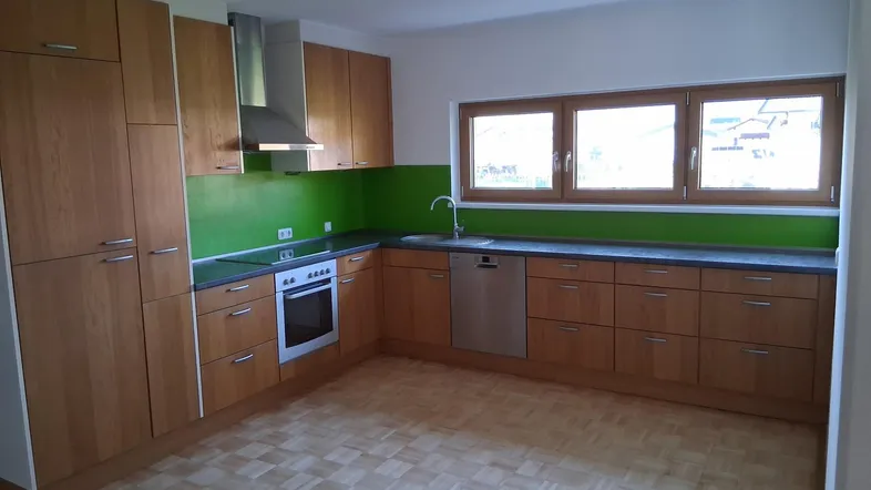 Moderne Einbauküche mit Holzfronten, grüner Rückwand, Edelstahlgeräten und Parkettboden.