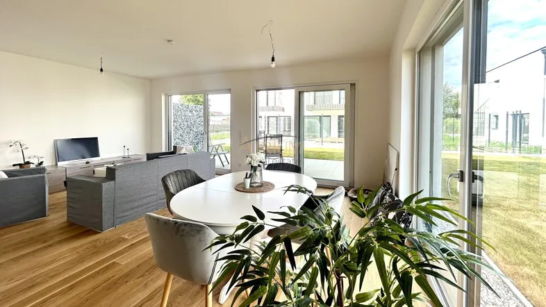 Heller, offener Wohn-Essbereich mit Holzboden und Zugang zur Terrasse sowie Blick ins Grüne.
