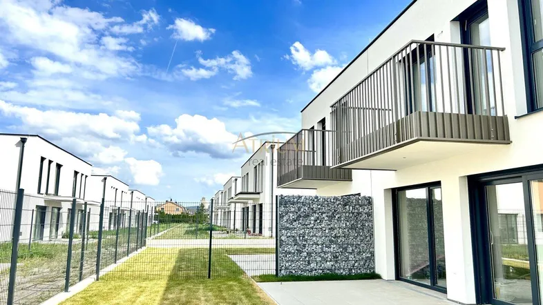Moderne Reihenhäuser mit Balkonen und Gärten unter blauem Himmel.